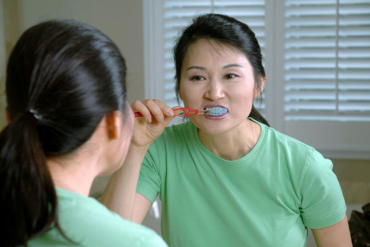 woman brushing her teeth in bathroom mirror